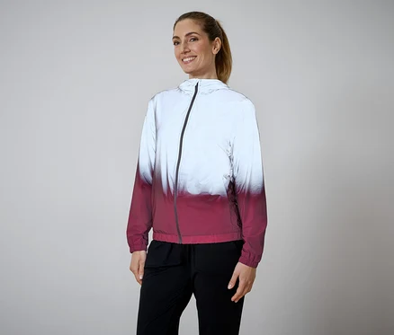 Une femme souriante portant une queue de cheval porte une veste zippée blanche et rouge et un pantalon noir.