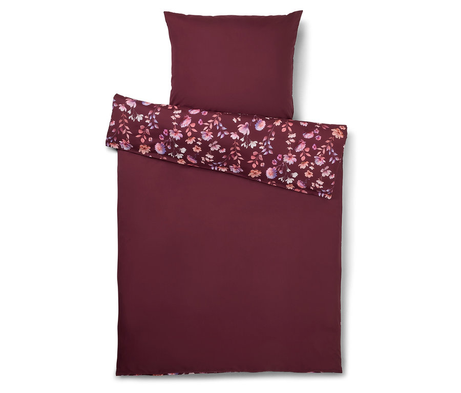 Des draps bordeaux à motifs floraux sont posés avec une taie d'oreiller sur un fond blanc.