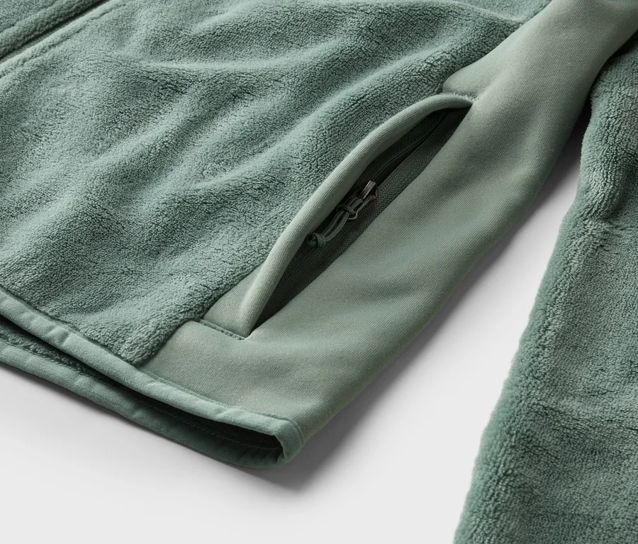 Gros plan d'une veste en polaire vert menthe avec une poche zippée sur la manche.