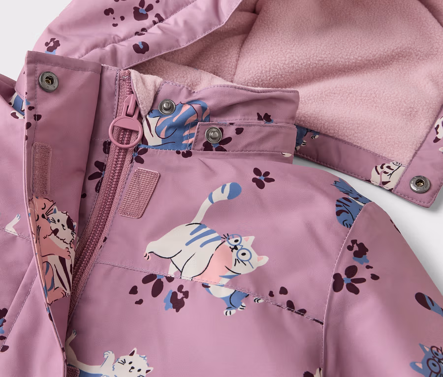 Gros plan d'une veste violette à motifs de chats et de fleurs, avec une fermeture éclair et une capuche doublée de polaire rose.