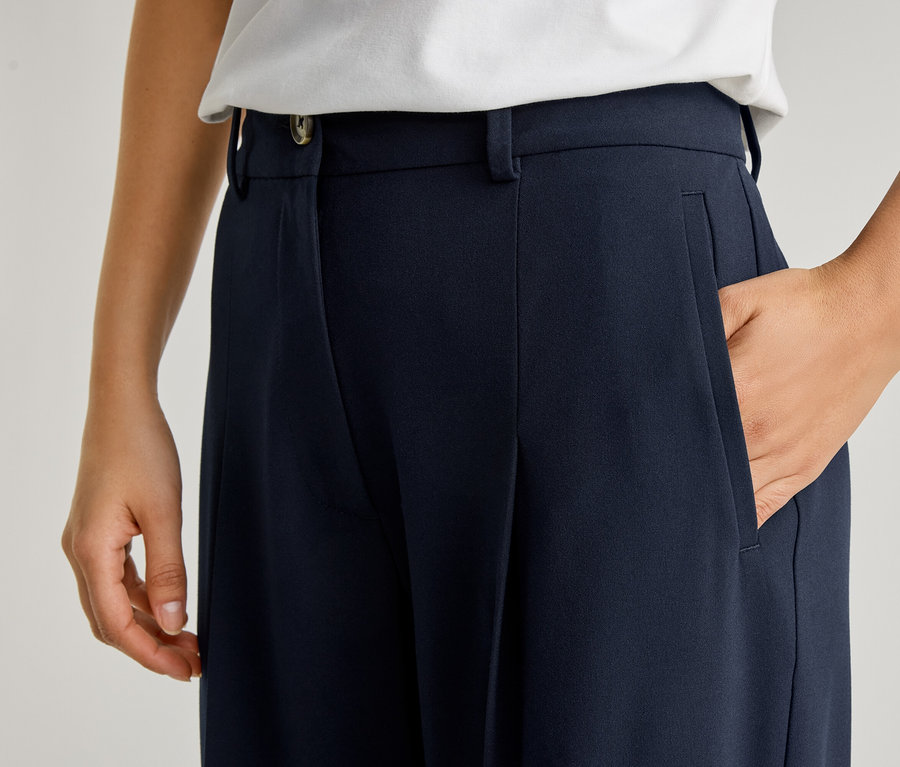 Gros plan d'une personne avec une main dans la poche d'un pantalon bleu marine avec des plis et un bouton.