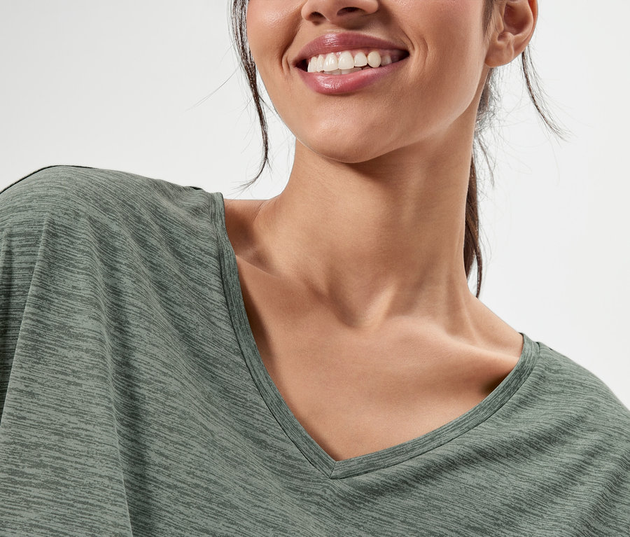 Gros plan d'une femme souriante portant un haut olive à col en V.