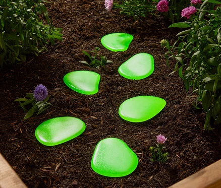 Des pierres décoratives vertes sont posées dans un parterre, entre des plantes.