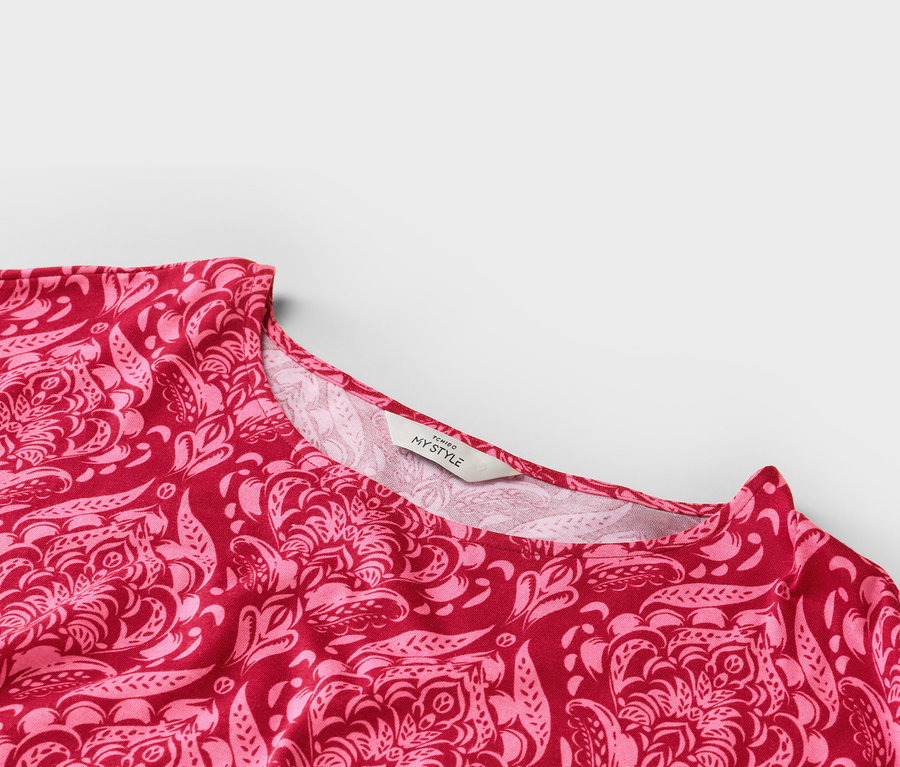 Gros plan du décolleté d'un haut à motifs rouge et rose avec une étiquette 'TCHIBO MY STYLE'.