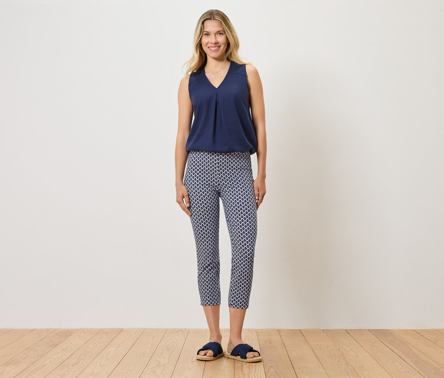 Femme debout portant un haut bleu, un pantalon à motifs et des pantoufles bleues.