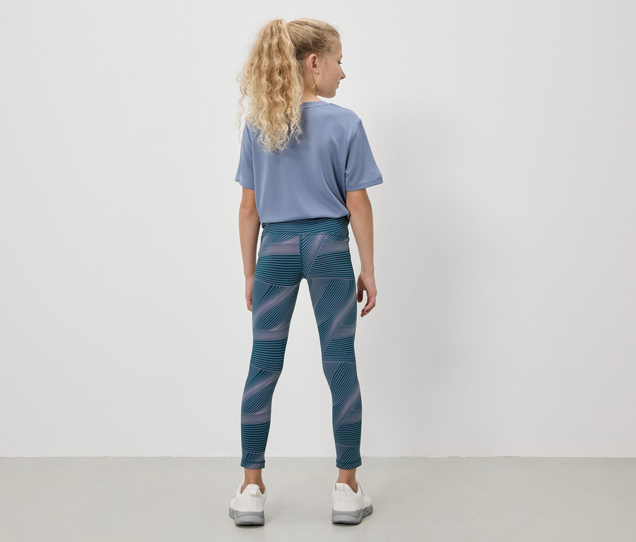 Une fille aux cheveux blonds porte un t-shirt bleu et un legging à motifs géométriques.