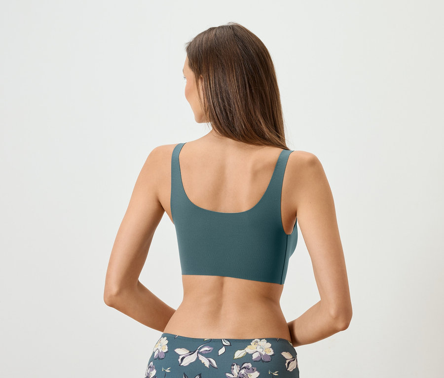 Vue de dos d'une femme aux longs cheveux bruns portant un soutien-gorge de sport pétrole et un legging à fleurs.
