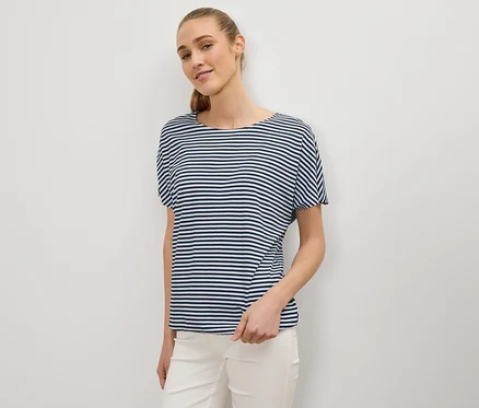 Femme avec queue de cheval portant un t-shirt rayé bleu et blanc et un pantalon blanc.