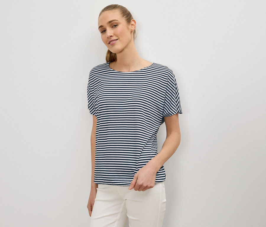 Femme avec queue de cheval portant un t-shirt rayé bleu et blanc et un pantalon blanc.