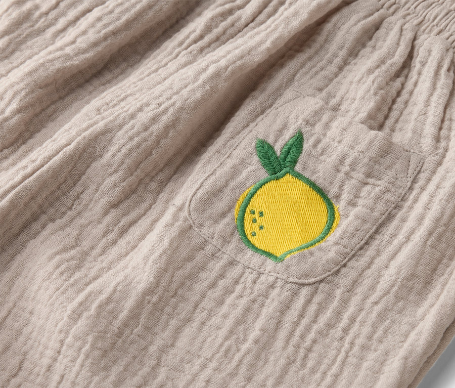 Gros plan d'un pantalon en tissu beige avec une ceinture élastique et une poche plaquée avec une broderie de citron jaune.