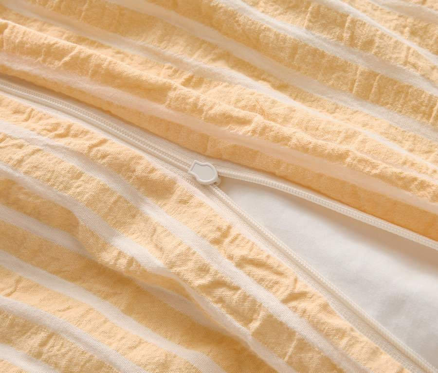 Gros plan d'une housse de couette partiellement ouverte avec un motif rayé jaune et blanc et une fermeture éclair blanche.