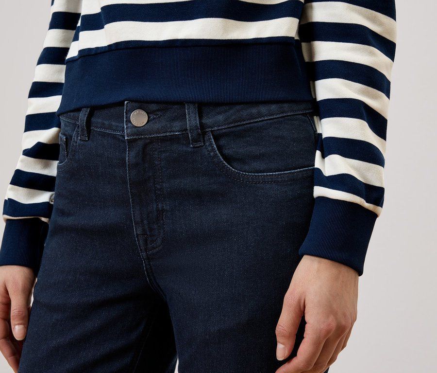Une personne porte un jean bleu foncé et un haut rayé bleu et blanc.