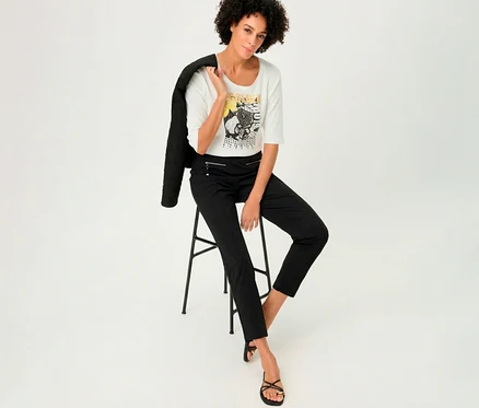 Femme assise sur un tabouret avec un T-shirt 3/4 Olsen, une veste sur l'épaule.