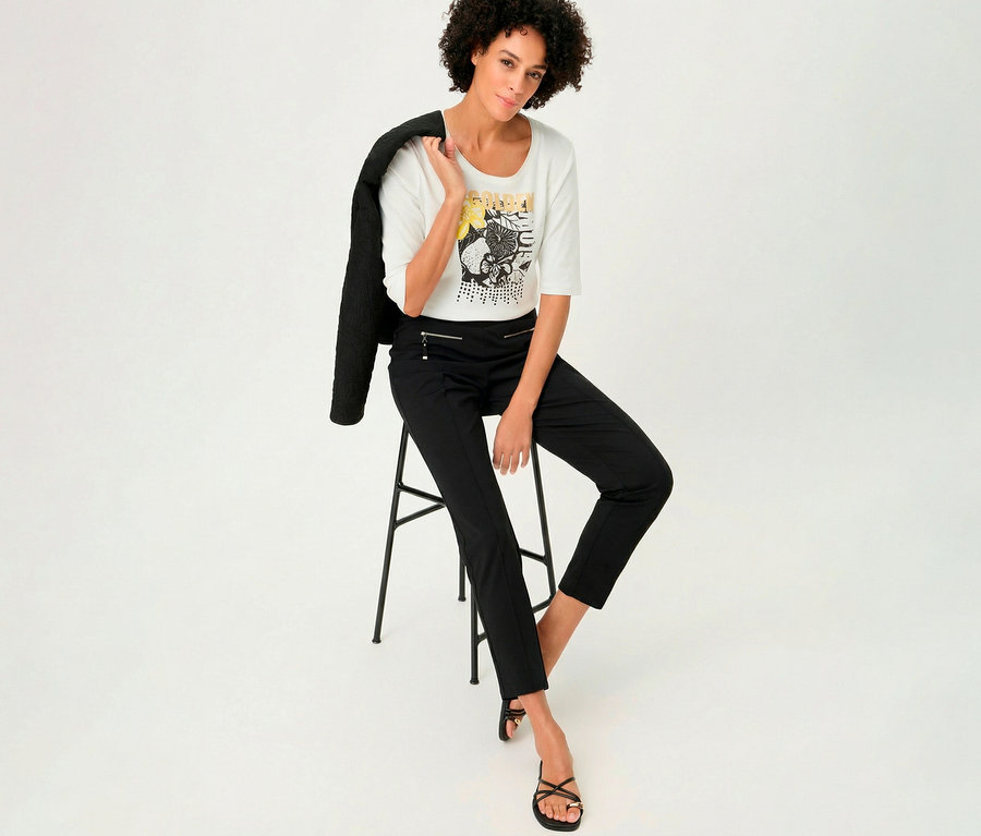 Femme assise sur un tabouret avec un T-shirt 3/4 Olsen, une veste sur l'épaule.