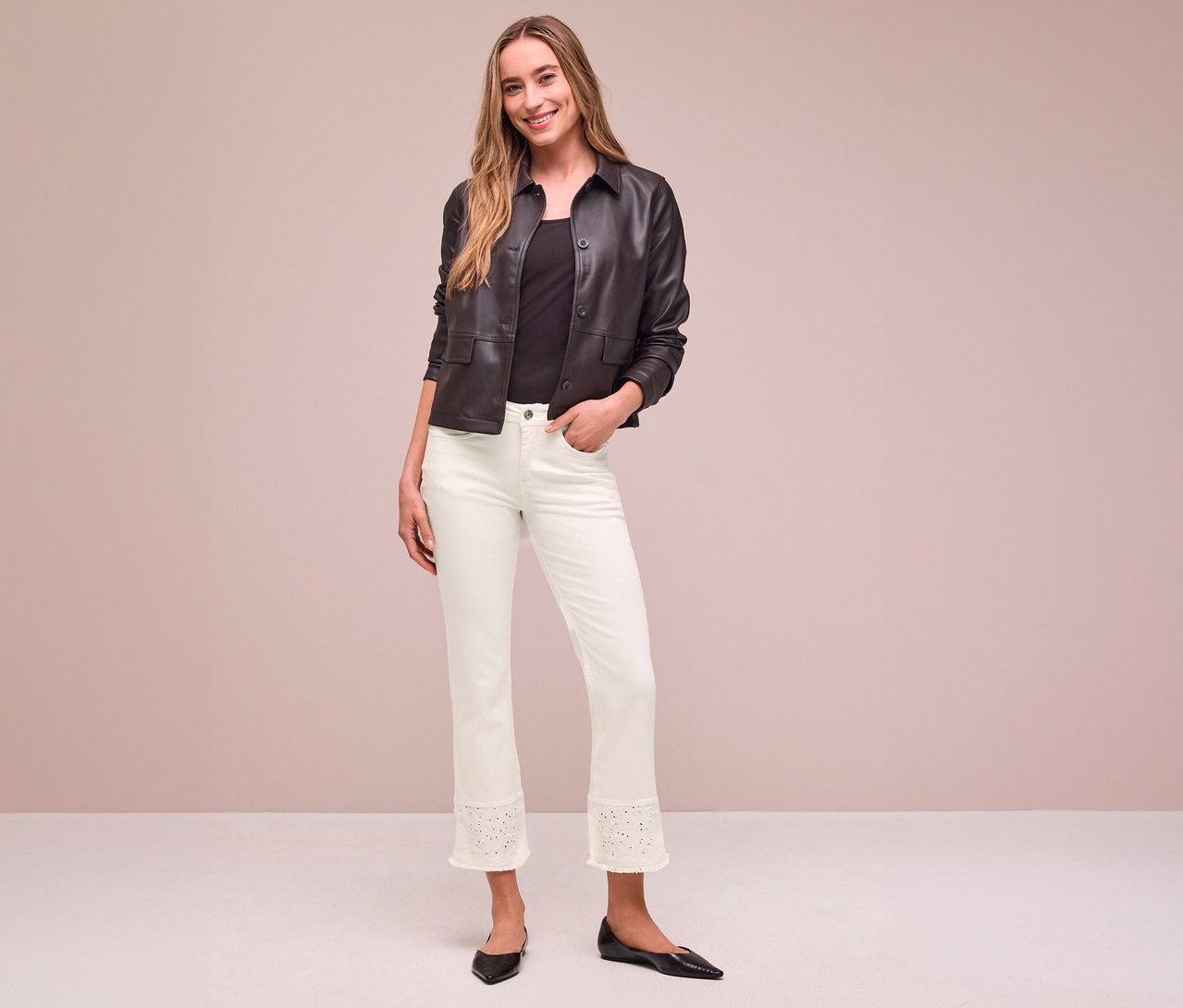 Femme souriante portant une veste marron foncé, un haut noir et un Jeans Street One clair avec un ourlet perforé, une main dans la poche.