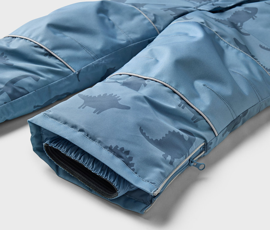 Gros plan sur le bas d'un pantalon bleu à motif de dinosaures avec une fermeture éclair sur la jambe.