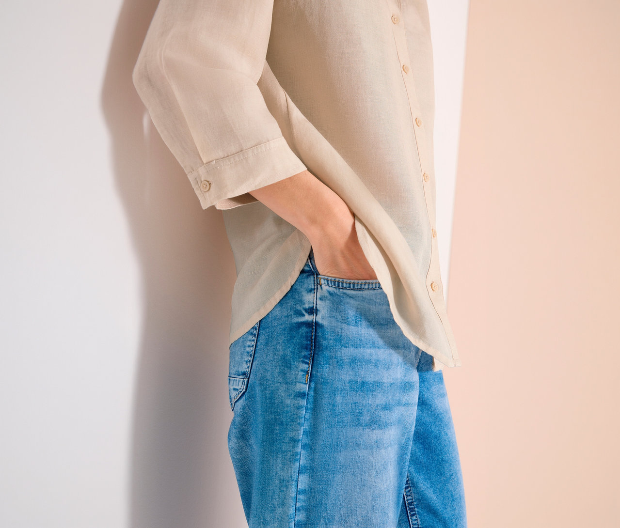 Personne portant un chemisier en lin beige et un jean bleu, la main dans la poche.