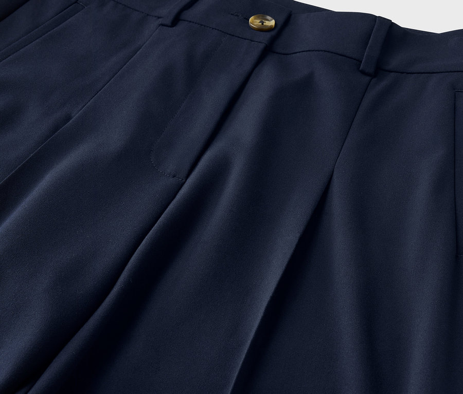 Gros plan sur un pantalon bleu marine avec des plis, un bouton et une poche.