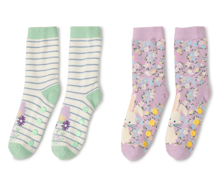 Deux paires de chaussettes antidérapantes pour enfants sont côte à côte. Une paire est rayée avec des fleurs, l'autre avec des fleurs et des lapins.