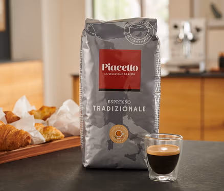 Un paquet d'Espresso Tradizionale Piacetto est posé sur une table à côté d'une tasse d'espresso et d'un plateau de croissants.