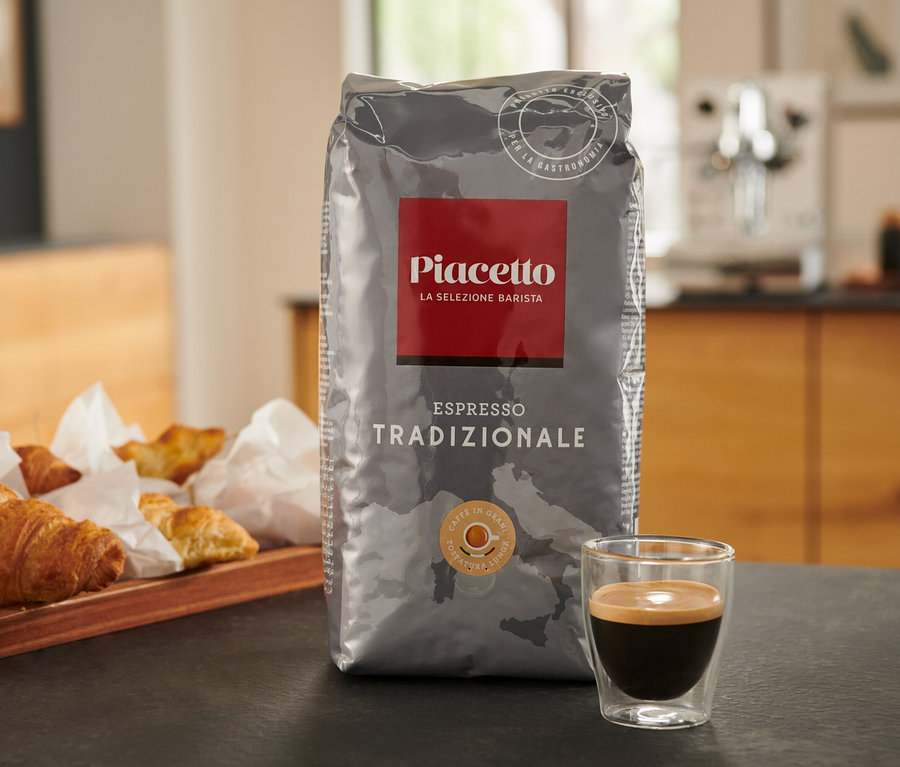 Un paquet d'Espresso Tradizionale Piacetto est posé sur une table à côté d'une tasse d'espresso et d'un plateau de croissants.