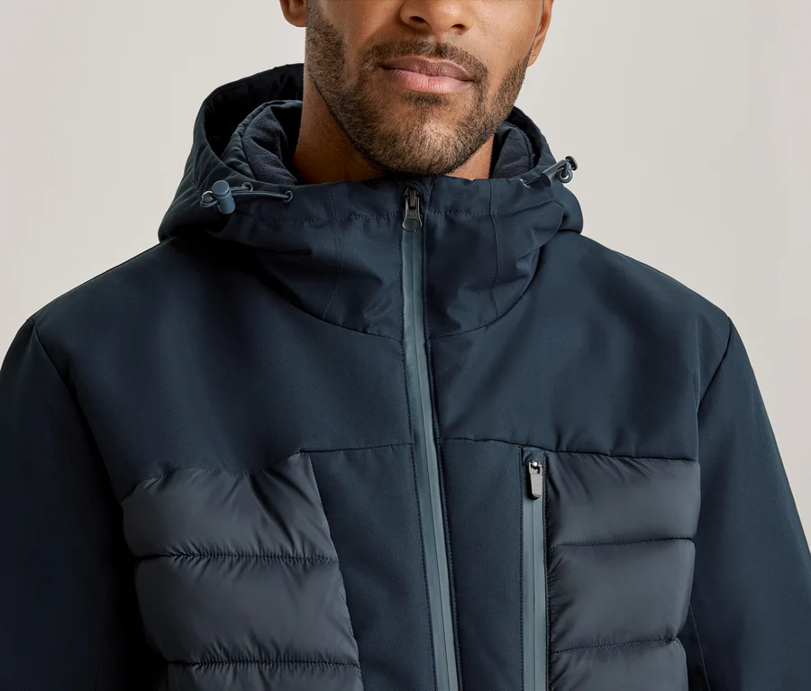 Homme portant une veste à capuche bleu foncé avec des sections rembourrées sur la poitrine et une poche zippée.