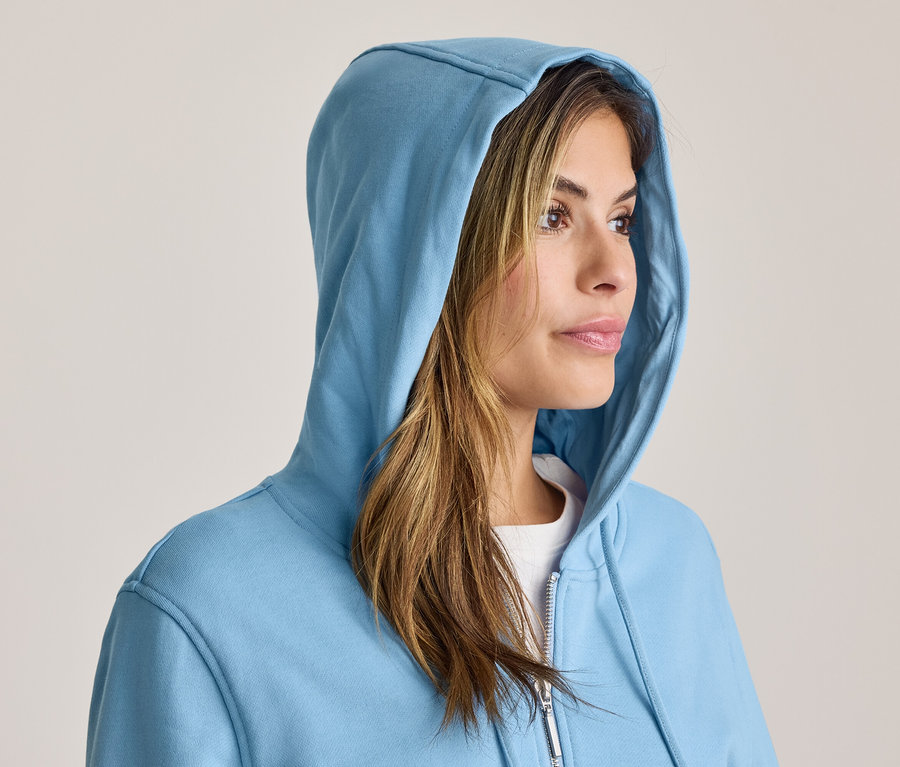 Femme portant un sweat à capuche bleu, regardant vers la droite, ses cheveux bruns sont visibles.