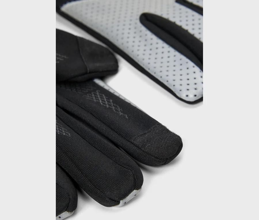 Gros plan sur des gants noirs avec des paumes perforées gris clair et des doigts côtelés, montrant un motif subtil sur le dos de la main.