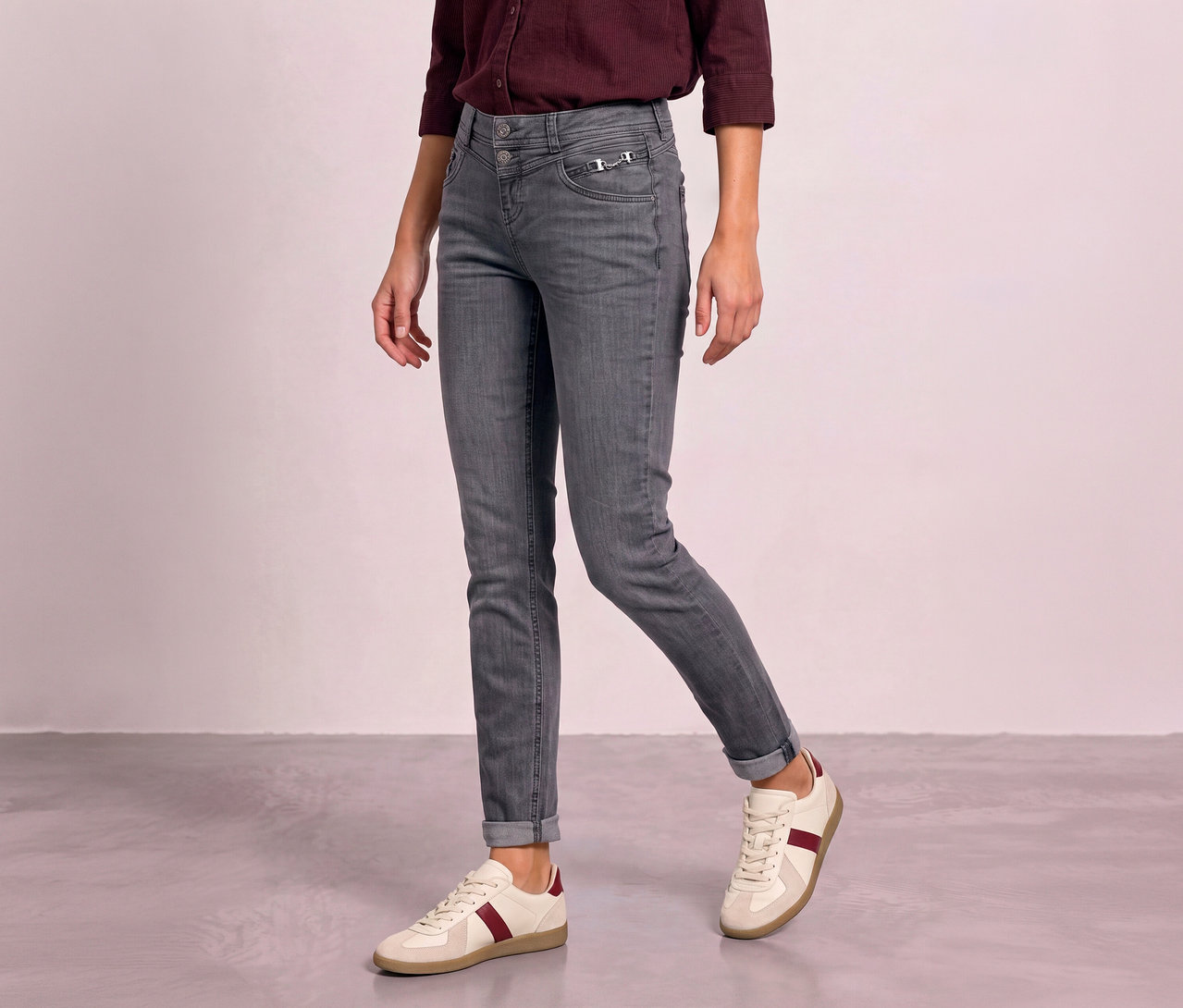 Personne portant un jean Street One gris avec des chevilles retroussées et des baskets crème à rayures bordeaux.