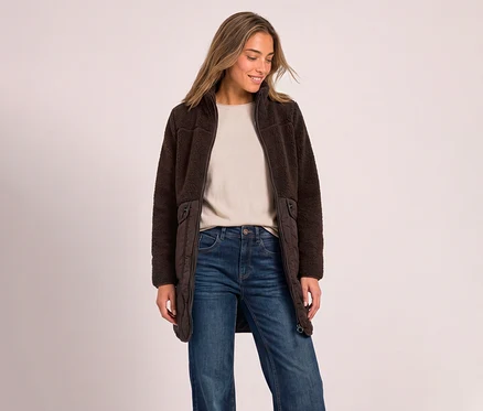 Une femme porte un manteau en teddy Street One marron foncé ouvert, un haut beige et un jean bleu.