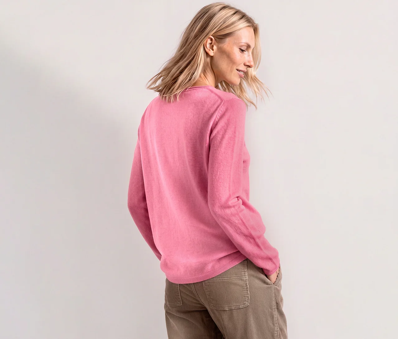 Femme blonde portant un pull en maille Street One rose pâle et un pantalon en velours côtelé marron clair, les mains dans les poches.