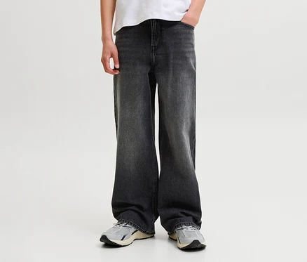 Personne portant un jean large gris foncé, un t-shirt blanc et des baskets gris clair, une main dans la poche.