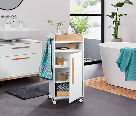 Dans une salle de bain, on trouve une armoire sous-lavabo blanche «Eklund» à deux tiroirs, un organisateur, un distributeur de savon liquide, un linge de bain en tissu éponge, 2 linges de toilette en jacquard, 2 linges de toilette en tissu éponge (anthracite), 2 boîtes en bambou, 2 pierres décoratives à LED et un chariot d’appoint pour salle de bains «Eklund».