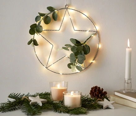 Un anneau à LED avec des branches artificielles est accroché au mur. Des bougies et des branches sont posées sur la commode.