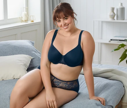 Femme assise sur un lit portant un soutien-gorge à armature bleu foncé.