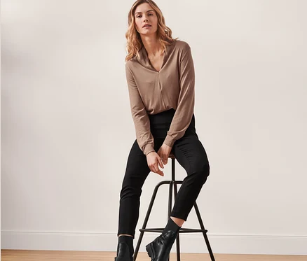 Une femme blonde est assise sur un tabouret de bar, portant un chemisier marron et un pantalon stretch noir.