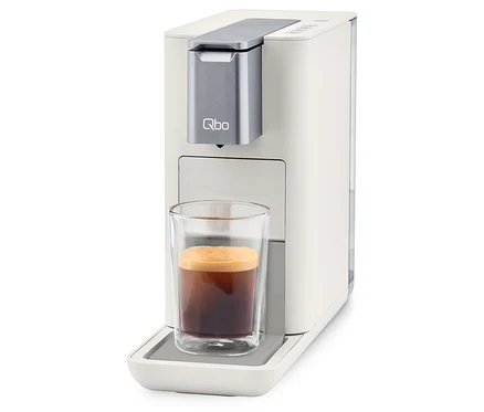 Machine à café Qbo ESSENTIAL Bright Sand avec une tasse de café.