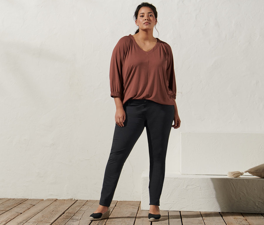 Femme posant dans une chemise couleur terre cuite avec des fronces, un jegging et des espadrilles à talon compensé.