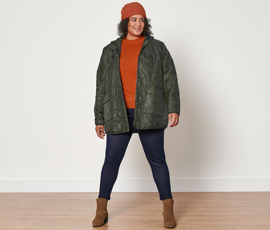 Une femme pose face à la caméra et porte un pull en maille, une veste matelassée, un legging doublé à l’aspect jean, un bonnet en maille et des bottines en cuir velours.