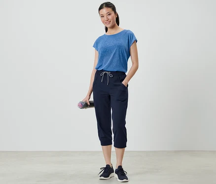 Femme tenant un tapis de yoga et portant un pantalon de sport 3/4.