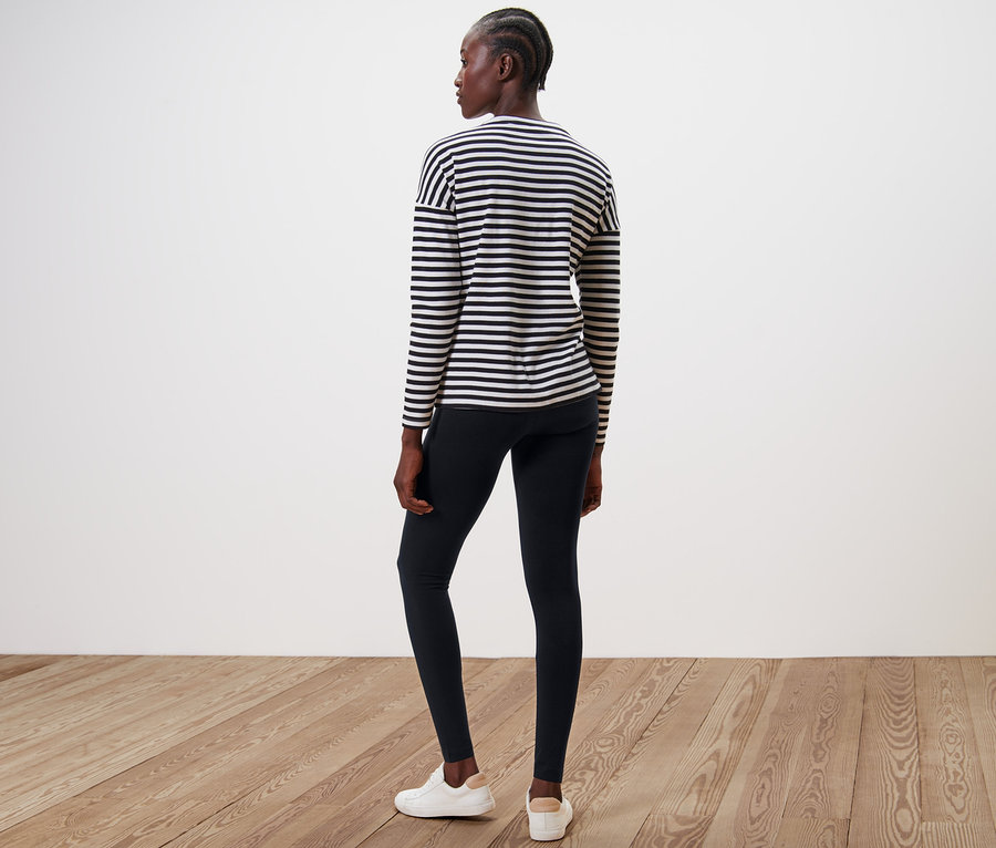 Une femme, vue de dos, porte un legging noir et un haut rayé.