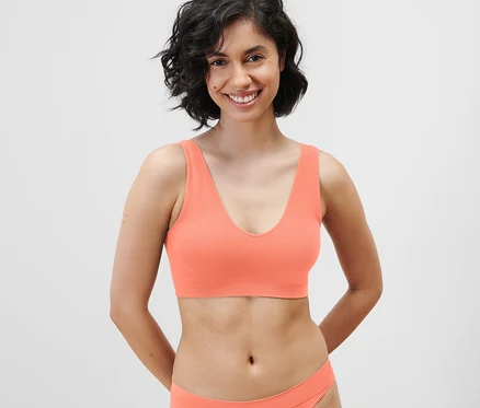 Une femme souriante porte un bustier sans couture de couleur papaye.