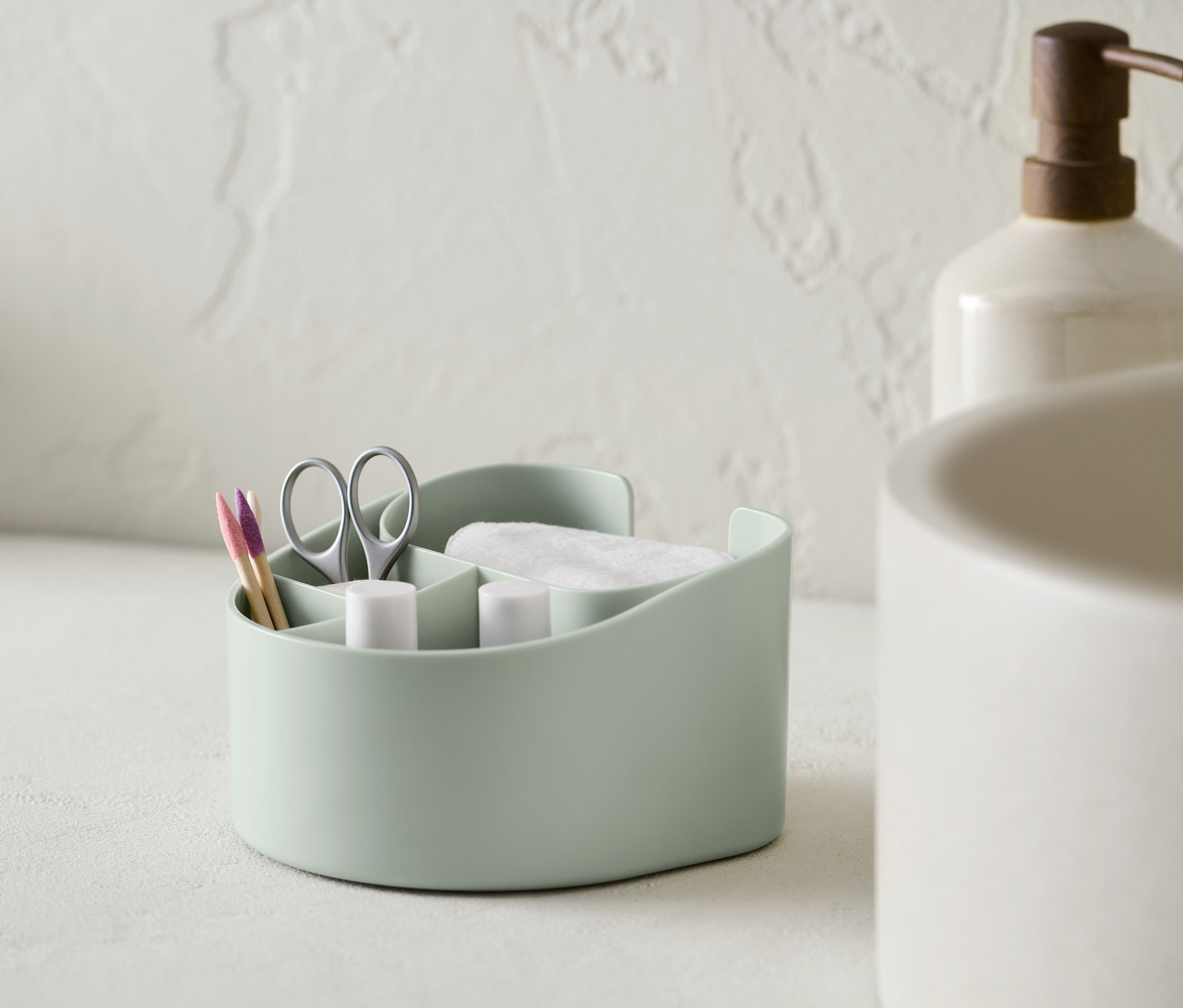 Un organiseur de cosmétiques vert clair avec des cotons, des ciseaux et des cotons-tiges.