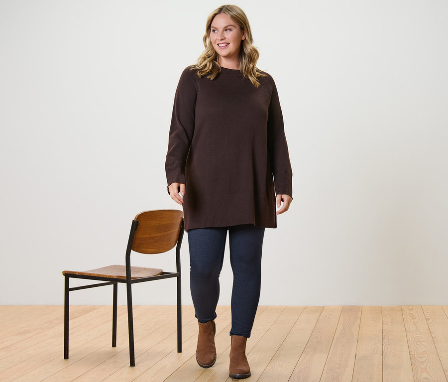 Une femme marche et porte un long pull en maille marron foncé et un legging doublé à l’aspect jean.