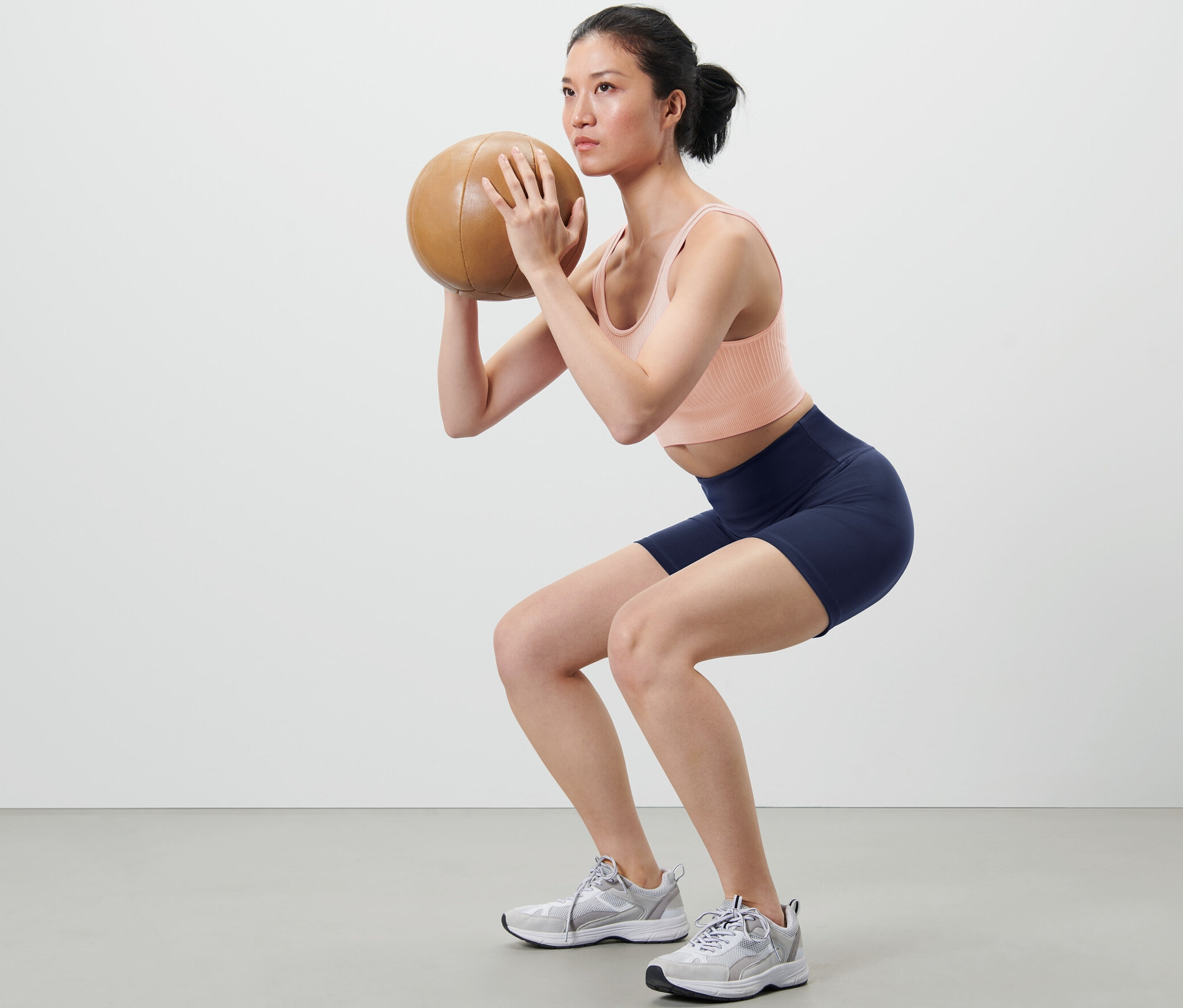 Femme faisant des squats avec un médecine-ball et portant un collant de sport court.