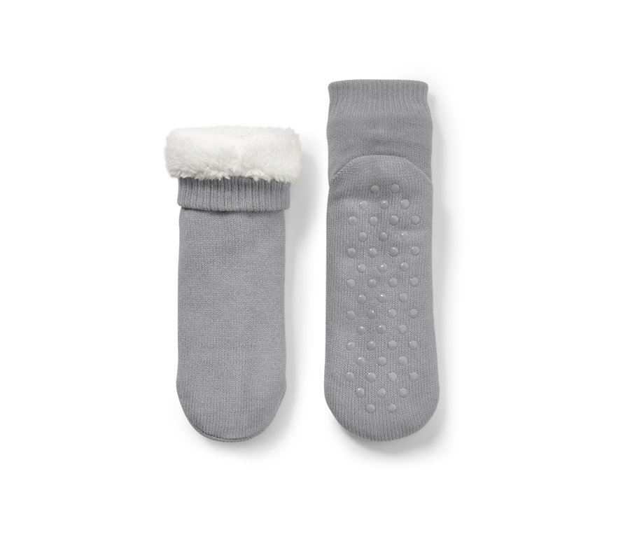 Deux chaussons-chaussettes gris, un avec bordure en peluche blanche, l'autre avec picots antidérapants.