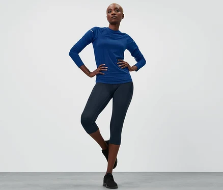 Femme posant en tenue de sport, portant un corsaire de sport bleu marine.