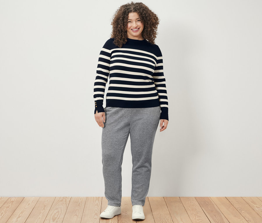 Une femme porte un pull en maille fine rayé bleu foncé et un pantalon de jogging.