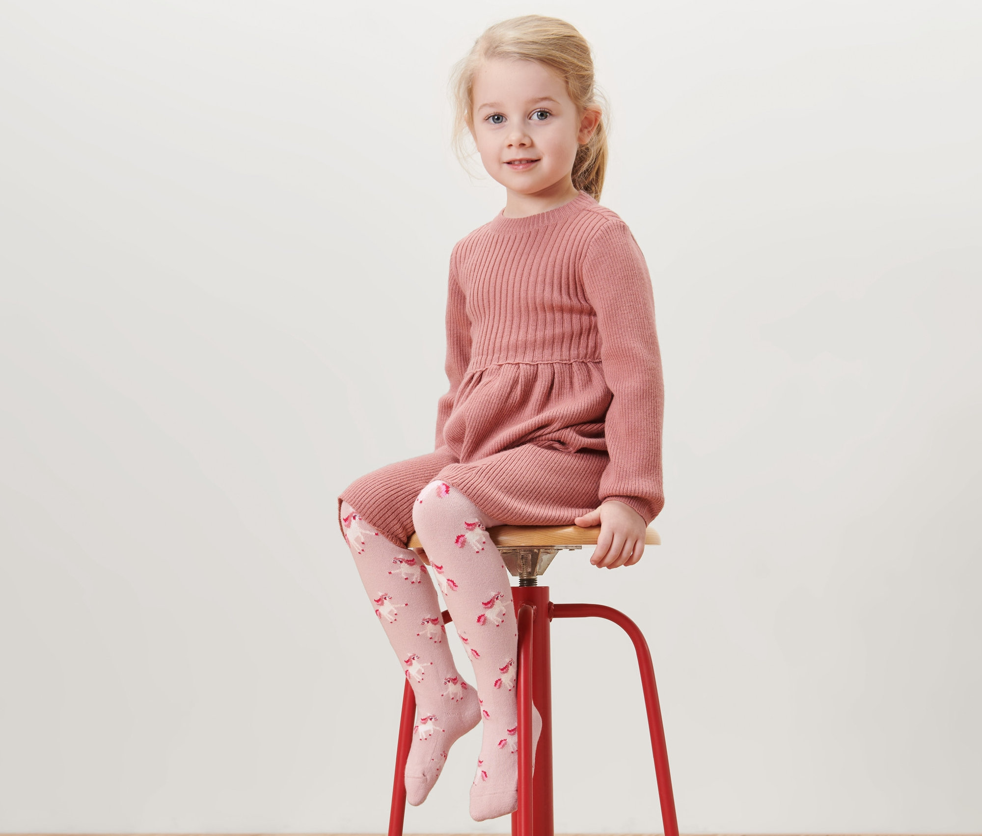 Fille assise sur un tabouret rouge portant une robe rose et 5 collants en coton, rhinocéros.
