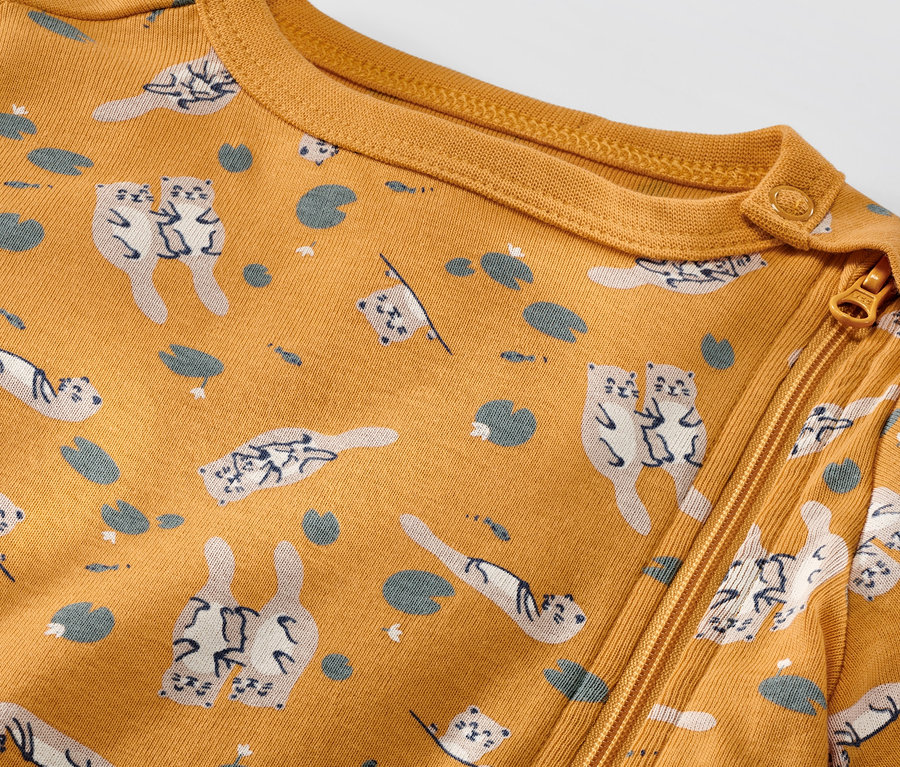 Gros plan sur un pyjama jaune pour bébé avec fermeture éclair et motif loutre et oie.